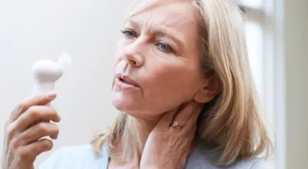 Femme blonde utilisant un petit ventilateur pour soulager les bouffées de chaleur de la préménopause. Elle a l'air inconfortable.