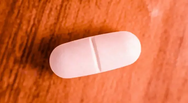 Comprimé blanc sur fond orangé. Une pilule de magnésium marin, attention aux effets secondaires.