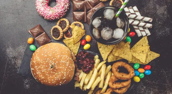 Un assortiment de 9 aliments mauvais pour les yeux : beignets, chocolat, tartes, nachos, soda, frites, oignons frits, bonbons et un hamburger.