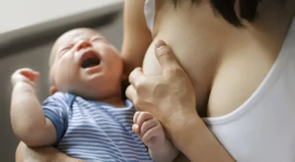Bébé pleure pendant l'allaitement. Une mère tient son enfant, possiblement pour soulager des symptômes de mastite.