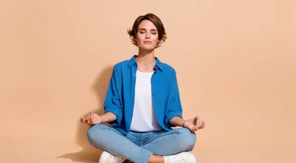 Femme en tenue décontractée, assise en tailleur, les yeux fermés, pratiquant la méditation.