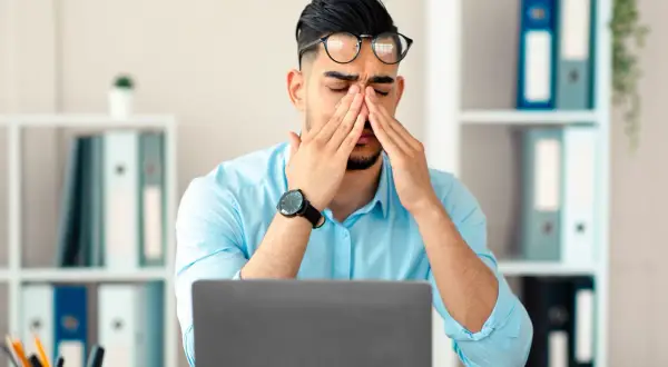 Homme fatigué au bureau, se frottant les yeux devant son ordinateur. Que faire contre la fatigue ?