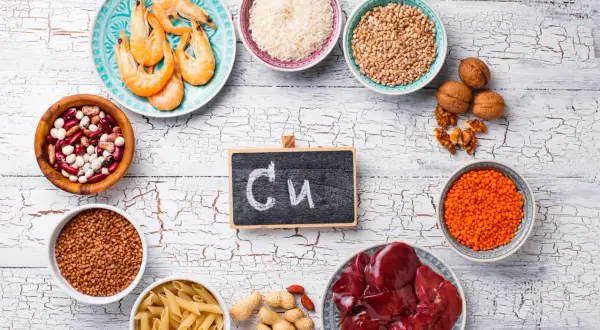 Assiette de crevettes, bols de riz, lentilles, haricots, pâtes, cacahuètes, noix, foie et un tableau noir avec "Cu" pour les cuivre bienfaits.