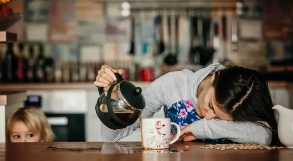Une femme, accablée par une grosse fatigue soudaine, essaie de se servir un café. Un enfant la regarde, perplexe.