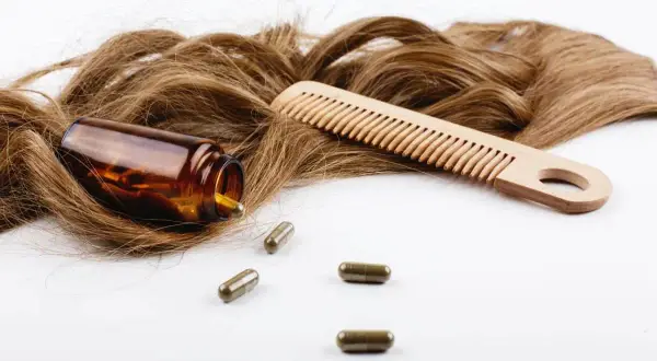 Chevelure brune, peigne en bois et pilules de biotine. Découvrez les biotine bienfaits pour des cheveux forts et brillants.