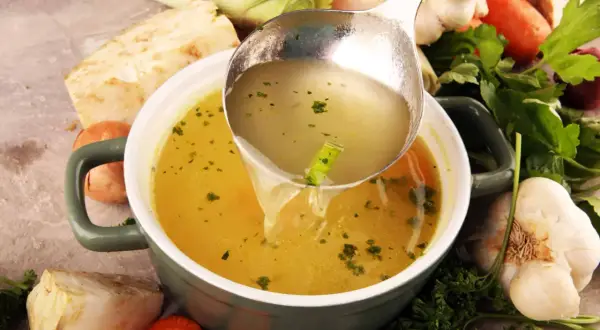 Un bouillon réconfortant, idéal pour soulager les maux d'estomac et la diarrhée. Des légumes frais entourent le bol.