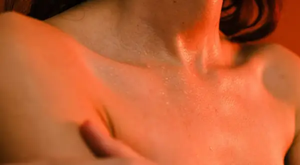 Peau moite sous une lumière orangée, évoquant les bouffées de chaleur ménopause combien de temps elles durent.