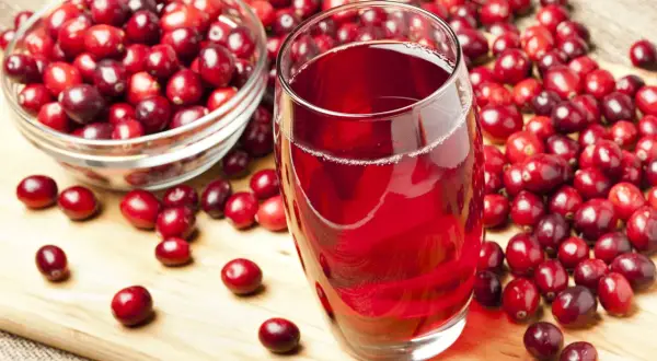 Un verre de jus de cranberry rouge vif, entouré de baies fraîches. Est-ce que le cranberry fait uriner ? Cette boisson est connue pour ses bienfaits.