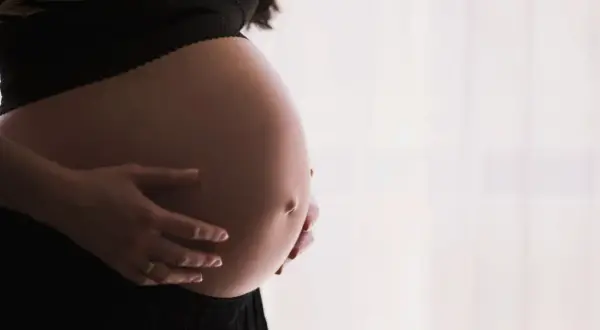 Gros plan sur le ventre arrondi d'une femme enceinte, ses mains le caressant. Un signe que la perte du bouchon muqueux approche.