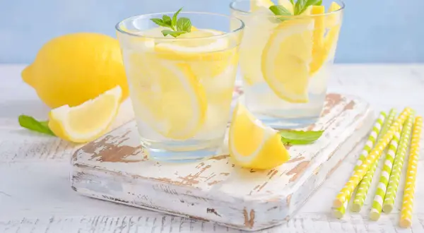 Deux verres de limonade pétillante avec des tranches de citron et des feuilles de menthe. Un citron entier et une tranche sont à côté. Parfait pour soulager les gaz intestinaux.