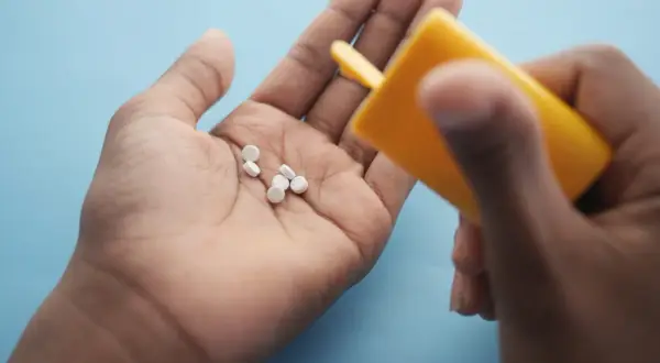 Main tenant une pilule dans sa paume, une main verse d'autres pilules d'un flacon jaune. Le maltitol peut présenter un danger.