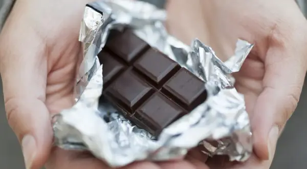 Mains tenant une tablette de chocolat noir déballée, rappelant ses bienfaits pour la santé et le plaisir.
