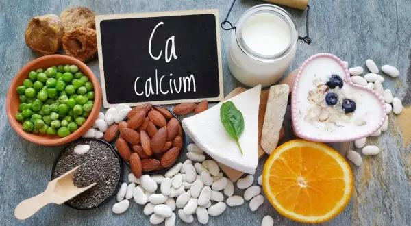 Assortiment d'aliments riches en calcium : lait, yaourt, fromage, amandes, haricots blancs, pois, figues séchées, graines de chia et orange.