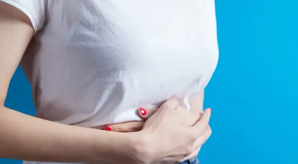 Une femme se tient les mains sur le ventre, ressentant une douleur en haut de l'estomac au milieu.