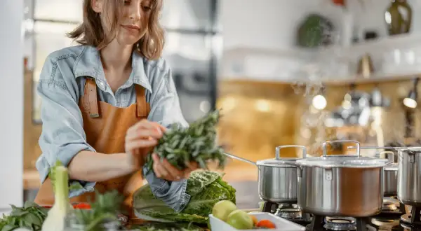 Une femme prépare des herbes fraîches dans une cuisine. La cuisson à haute température peut entraîner la destruction de certaines vitamines.