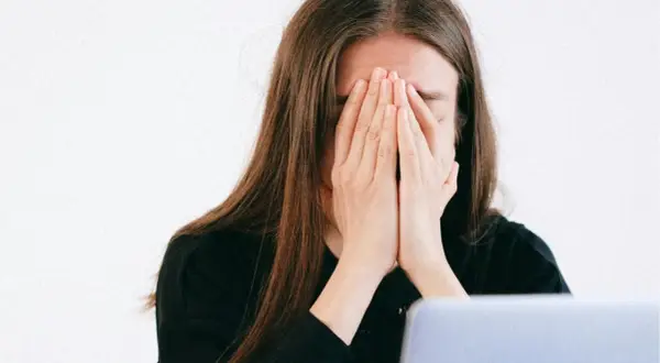 Une jeune femme, le visage caché par ses mains, exprime une **énorme fatigue** devant son ordinateur.