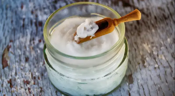 Un pot d'huile de coco avec une petite cuillère en bois. Attention, l'huile de coco danger pour la santé est un sujet de débat.