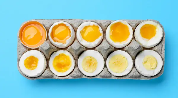 Dix œufs dans une boîte, du cru au dur, montrant la variation de la texture et de la couleur du jaune. Le **calorie œuf** change selon sa cuisson.