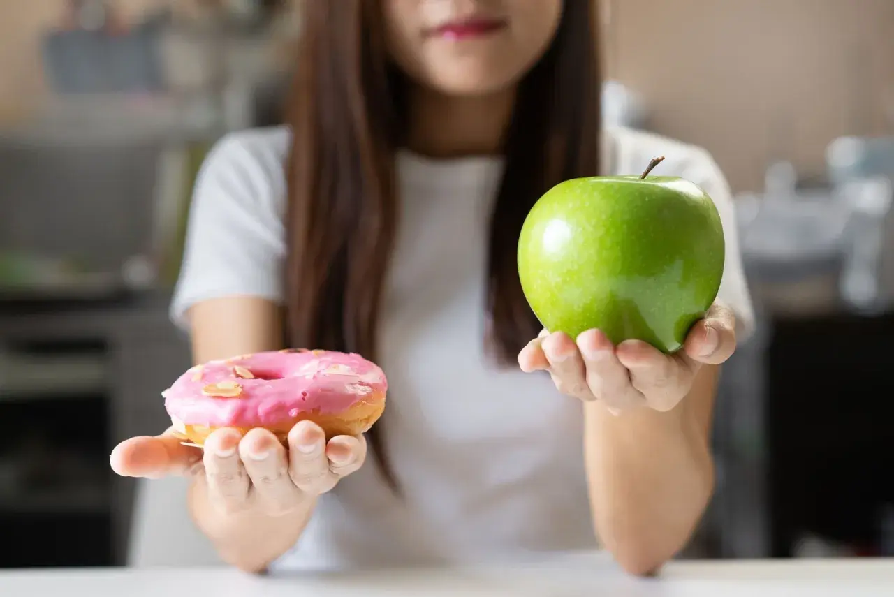Choix entre une pomme verte et un donut rose. Le donut est un exemple d'aliments mauvais pour la flore intestinale, contrairement à la pomme.