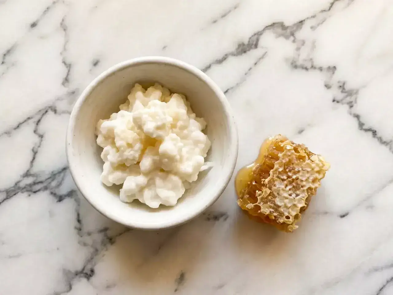 Un bol de kéfir crémeux à côté d'un morceau de nid d'abeille dégoulinant de miel. Attention, le kéfir peut présenter un danger s'il n'est pas préparé correctement.