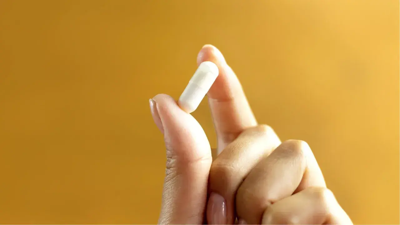Main tenue pour votre bien-être : 1g de vitamine C par jour, une capsule blanche tenue entre le pouce et l'index.