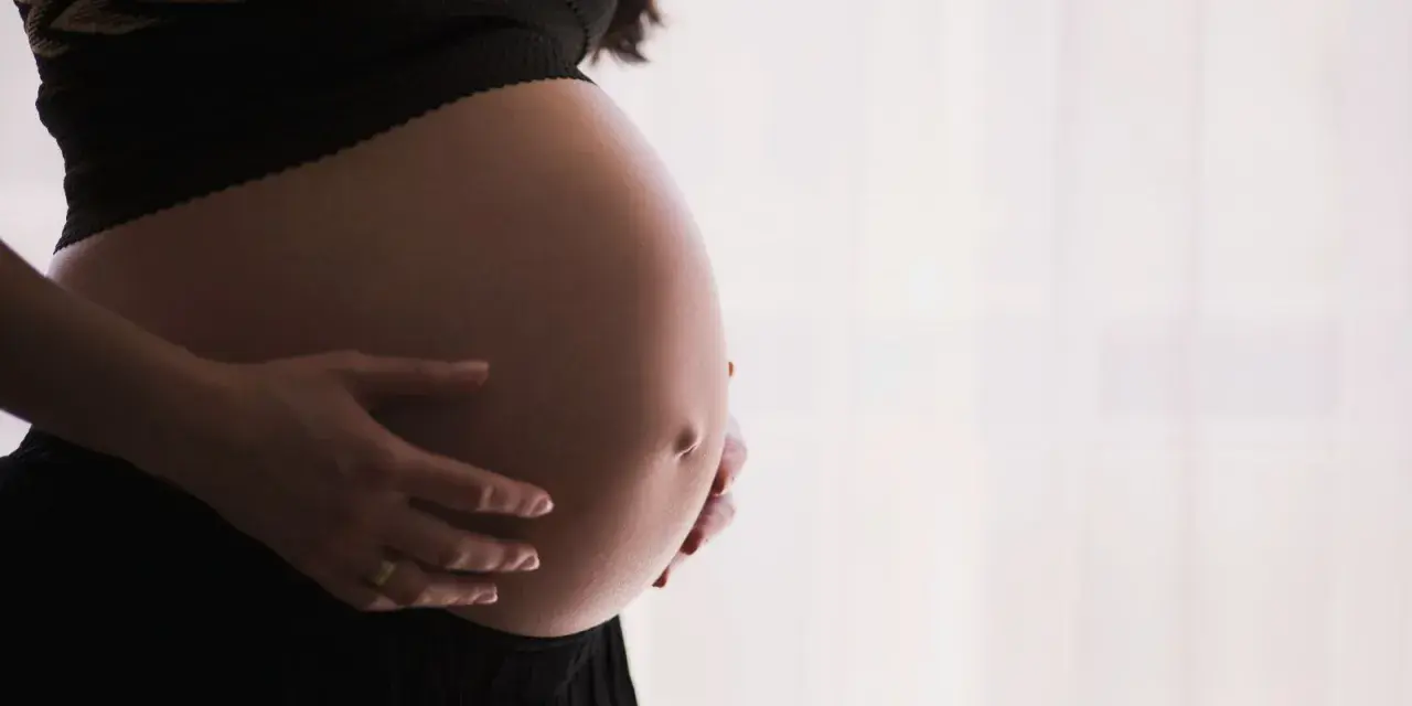 Gros plan sur le ventre arrondi d'une femme enceinte, ses mains le caressant. Un signe que la perte du bouchon muqueux approche.