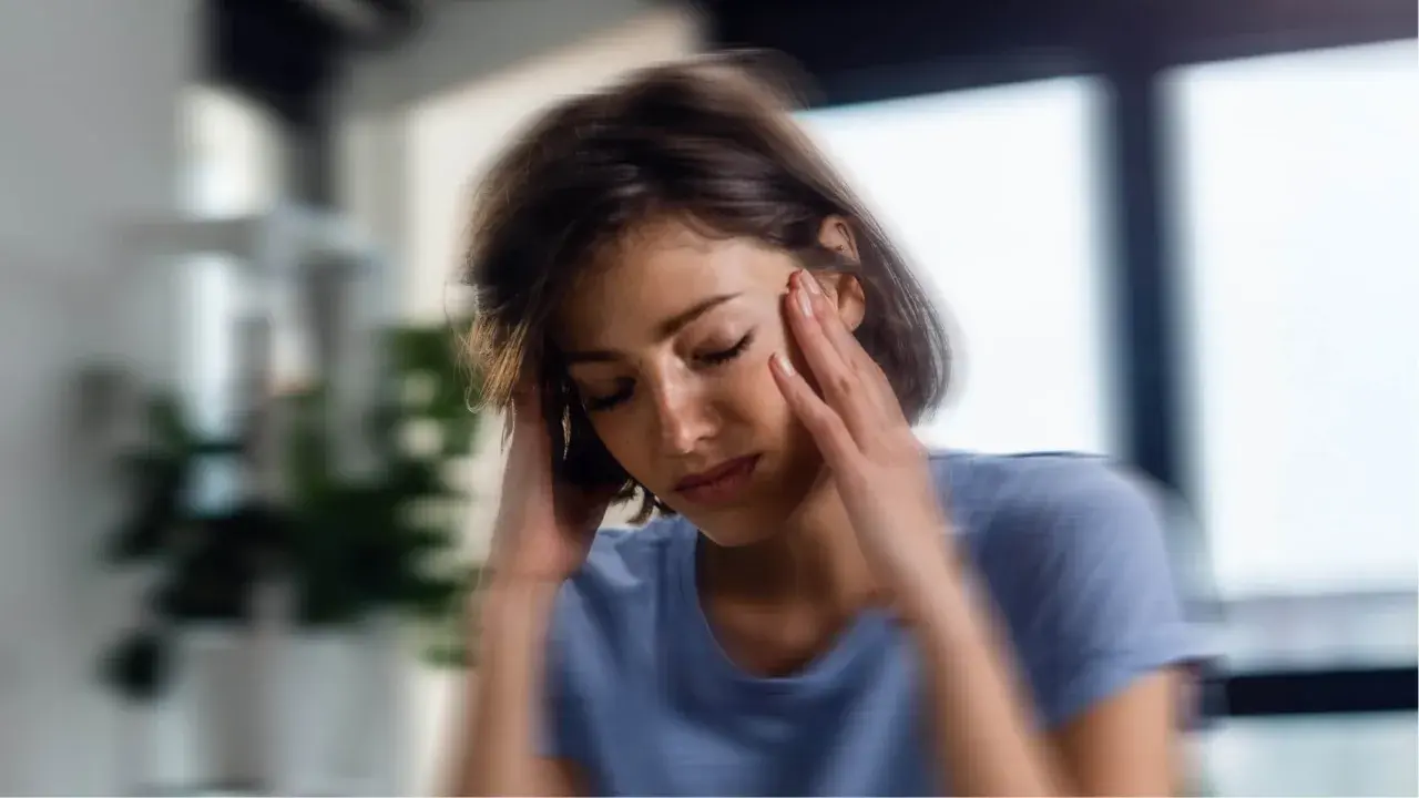 Femme se tenant la tête, les yeux fermés, signe d'une perte de vitalité.
