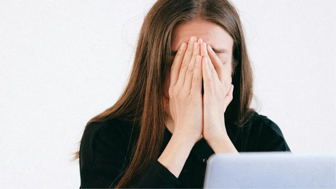 Une jeune femme, le visage caché par ses mains, exprime une **énorme fatigue** devant son ordinateur.