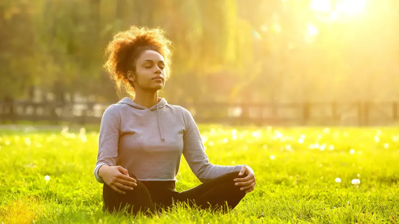 Une jeune femme médite dans un champ ensoleillé, une scène parfaite pour apprendre comment se détendre nerveusement.