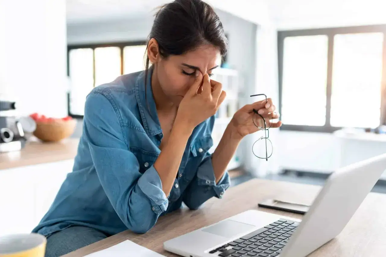 Femme épuisée, les mains sur le nez, devant un ordinateur. Le travail excessif peut causer une fatigue extrême.