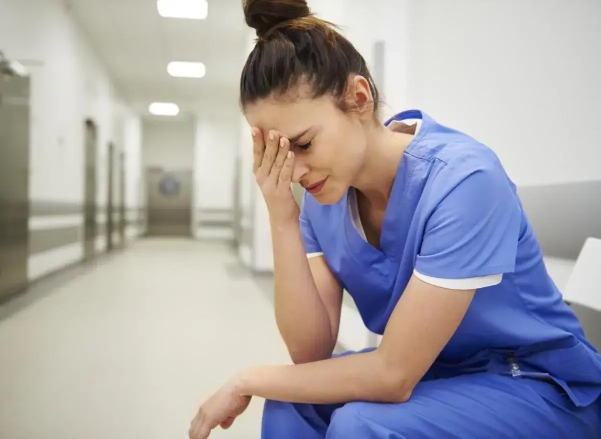 Infirmière en uniforme bleu, le visage dans les mains, accablée par un coup de fatigue soudain dans un couloir d'hôpital.