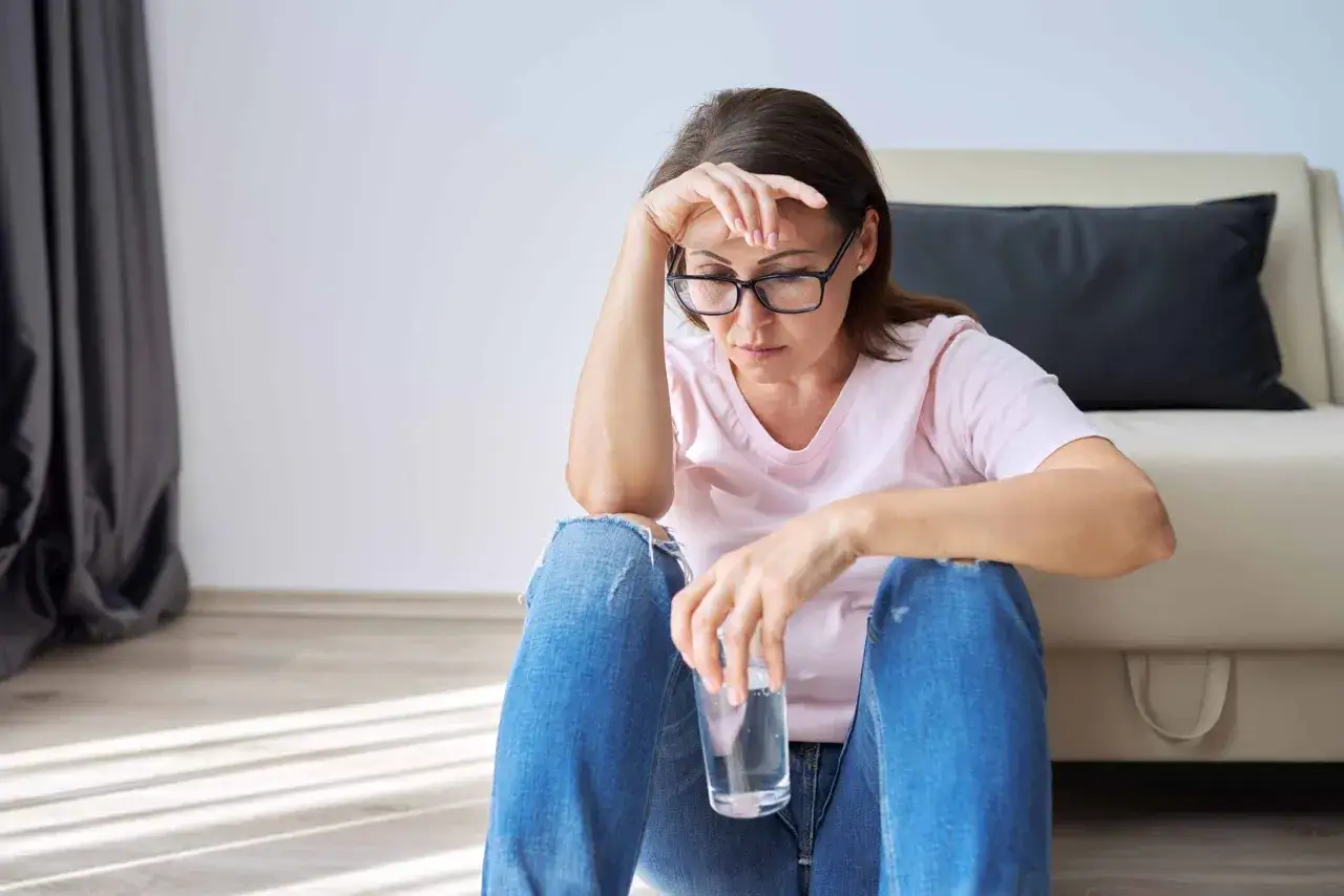 Femme fatiguée, se posant des questions sur les bouffées de chaleur ménopause combien de temps elles durent. Elle tient un verre d'eau.