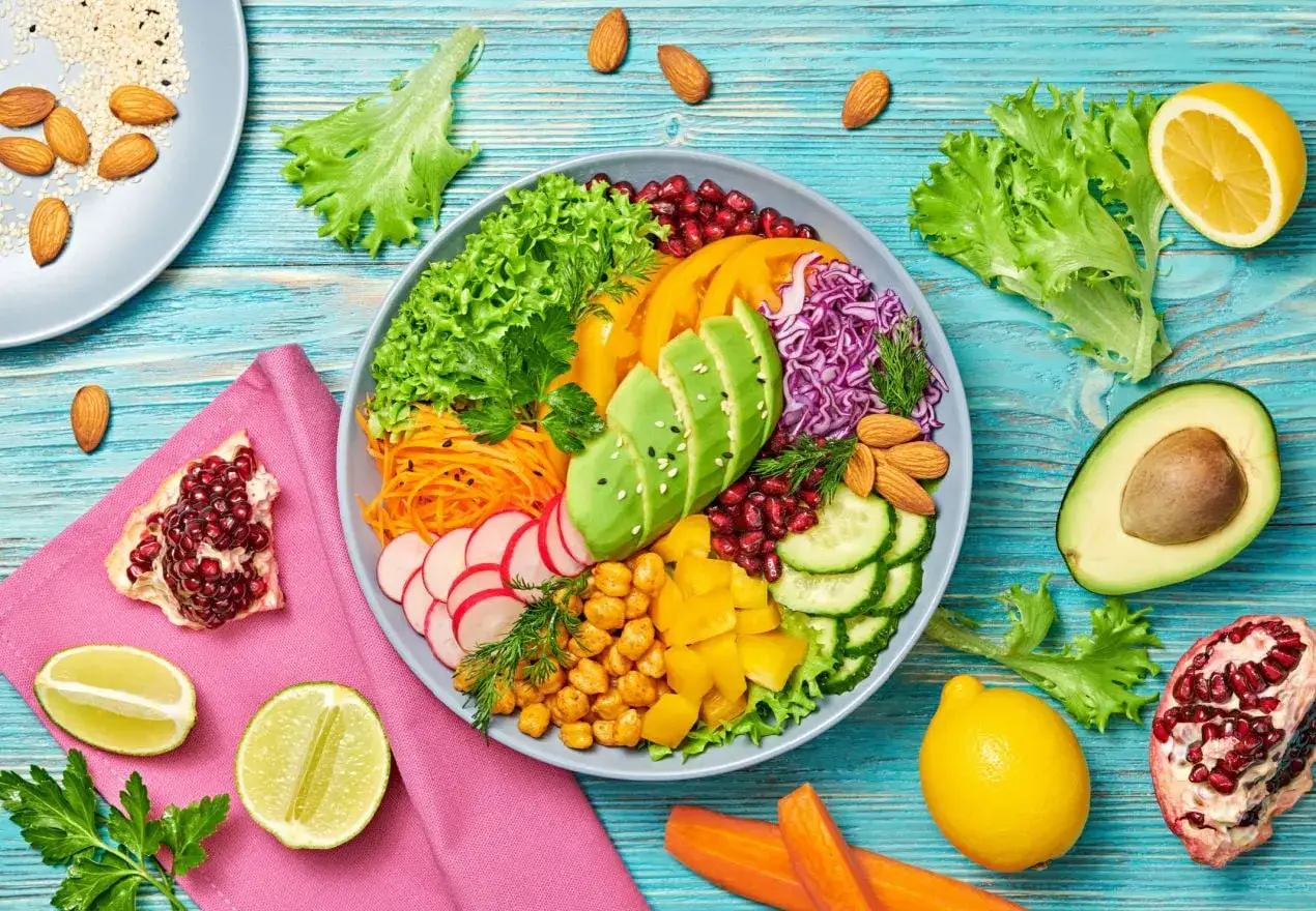 Un bol coloré avec avocat, carottes râpées, radis, pois chiches, grenade, concombre, chou rouge, et amandes. Parfait pour le top 20 des aliments chouchous du microbiote.