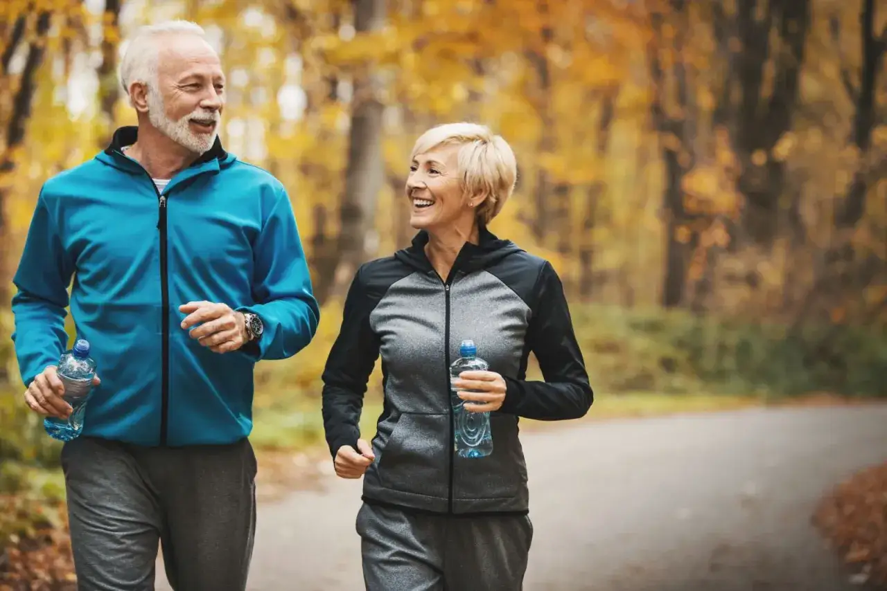 Couple souriant courant dans un parc automnal, découvrez comment ne plus être fatigué en 5 minutes grâce à l'exercice.