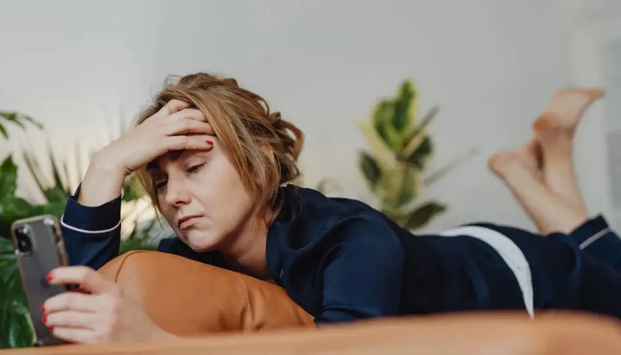 Femme fatiguée, la main sur le front, regardant son téléphone. L'endométriose affecte son humeur et son bien-être.
