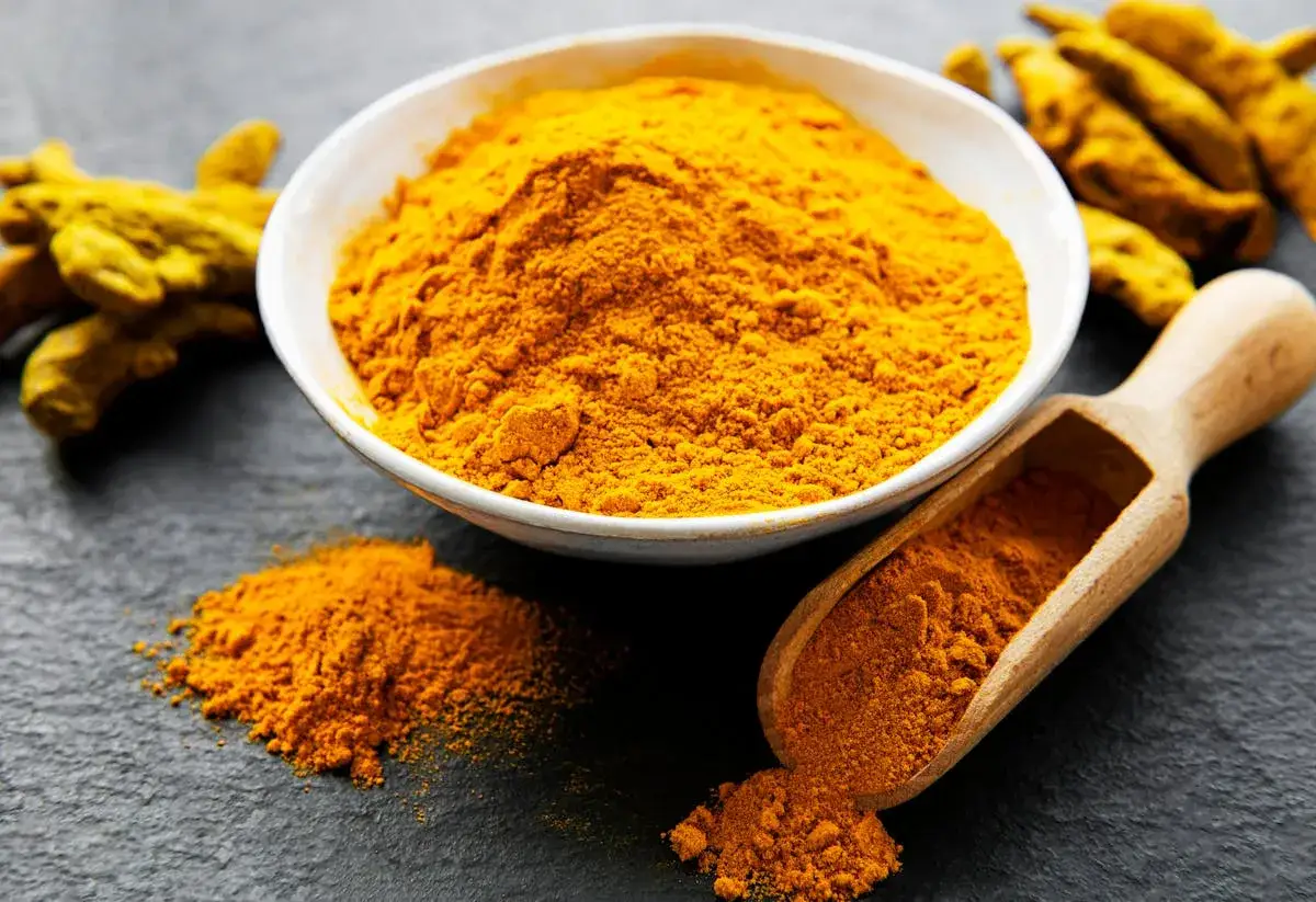 Poudre de curcuma vibrante dans un bol blanc, avec des racines de curcuma et une cuill&egrave;re en bois. Un ingr&eacute;dient naturel pour une femme enceinte.