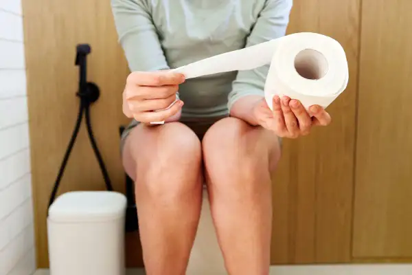 Une personne assise sur des toilettes tient un rouleau de papier toilette. La question est : est ce que les probiotiques constipent ?