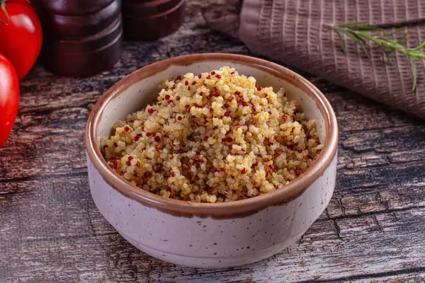 Bol rempli de quinoa, un aliment aux multiples quinoa bienfaits, avec des tomates et des épices en arrière-plan.