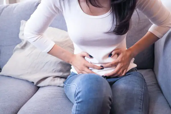 Femme assise sur un canapé, se tenant le ventre, possiblement à cause d'une inflammation de l'utérus.