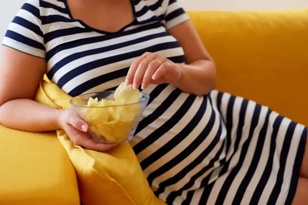 Une femme en robe rayée mange des chips dans un bol. Elle se demande : "J'ai mangé trop salé, que faire ?