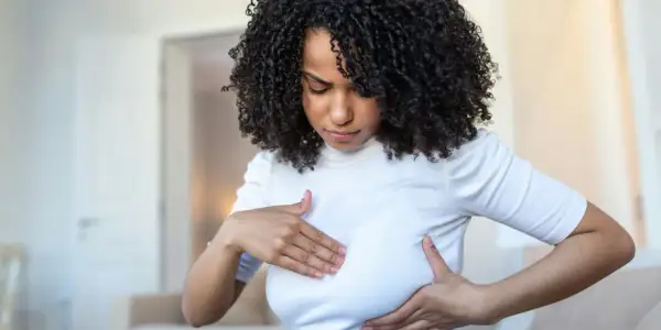 Femme aux cheveux bouclés examinant sa poitrine, inquiète des symptômes de mastite infectieuse.