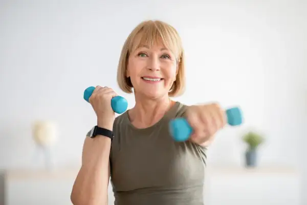 Femme souriante faisant du sport avec haltères bleus, un exemple de sport ménopause pour rester en forme.