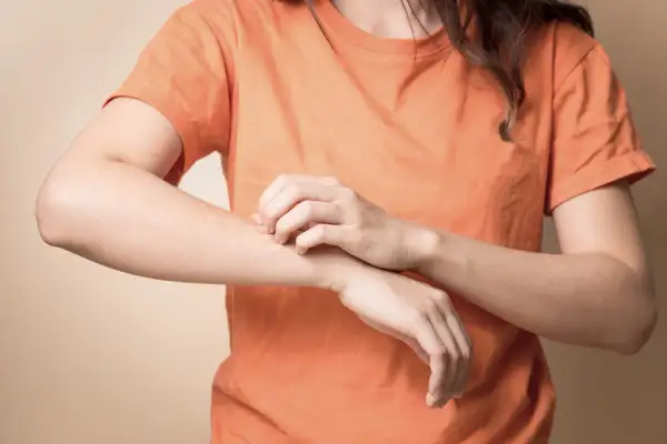 Une personne se gratte le bras, peut-être à cause d'une carence. Les vitamine b1 bienfaits incluent une peau saine.