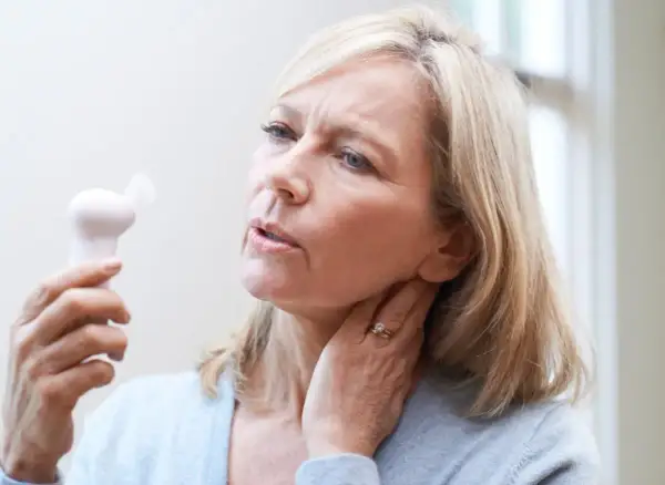 Femme blonde utilisant un petit ventilateur pour soulager les bouffées de chaleur de la préménopause. Elle a l'air inconfortable.
