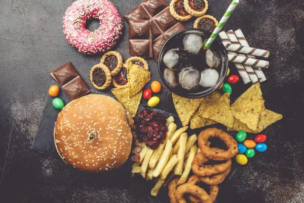 Un assortiment de 9 aliments mauvais pour les yeux : beignets, chocolat, tartes, nachos, soda, frites, oignons frits, bonbons et un hamburger.