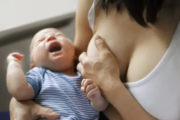 Bébé pleure pendant l'allaitement. Une mère tient son enfant, possiblement pour soulager des symptômes de mastite.