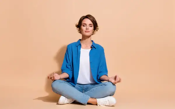 Femme en tenue décontractée, assise en tailleur, les yeux fermés, pratiquant la méditation.