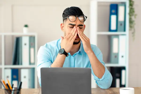 Homme fatigué au bureau, se frottant les yeux devant son ordinateur. Que faire contre la fatigue ?