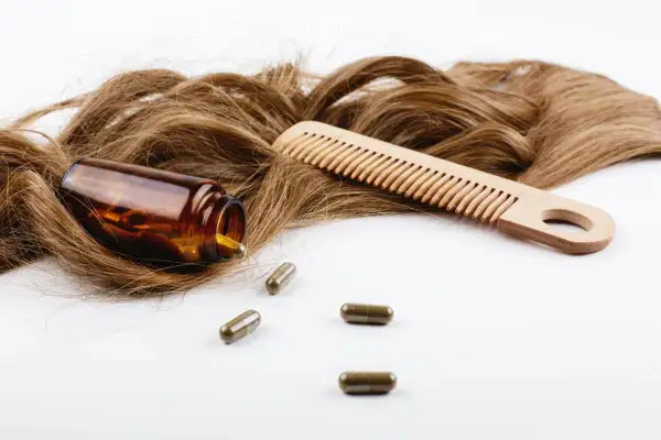 Chevelure brune, peigne en bois et pilules de biotine. Découvrez les biotine bienfaits pour des cheveux forts et brillants.