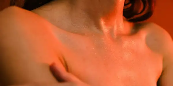 Peau moite sous une lumière orangée, évoquant les bouffées de chaleur ménopause combien de temps elles durent.